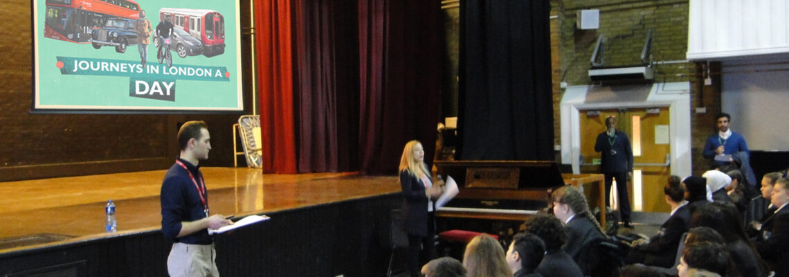 Fare City giving a presentation at the front of a school assembly.