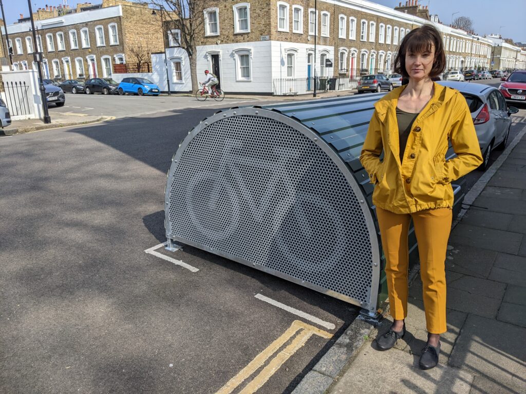 A lady standing alongside a cycle hangar on a residential street in the London borough of Islington.